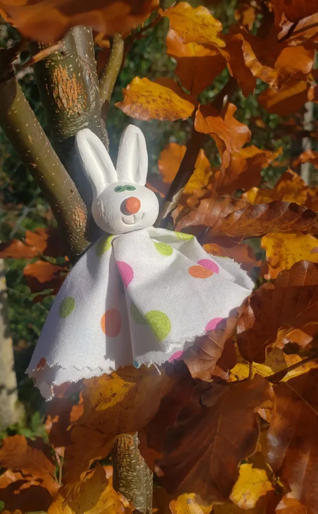 marionnette lapin en céramique et tissu posée sur un lit de feuilles mortes.