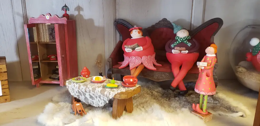 Trois personnages en céramique créés par Laure Laforge installés dans une scène représentant un salon miniature avec canapé, table basse, armoire et des accessoires en poterie artisanale originale.